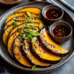 Steamed kabocha squash slices arranged on a ceramic plate, drizzled with a ginger-soy dressing, garnished with sesame seeds and green onions, served alongside dipping sauces.