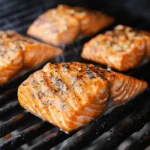 Fresh salmon fillets on a pellet grill, beautifully seared with a golden crust, seasoned with herbs and spices, and infused with smoky flavor.